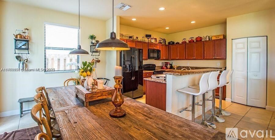 A kitchen with a wooden table and chairs in the foreground and a refrigerator, microwave, and cabinets in the background.