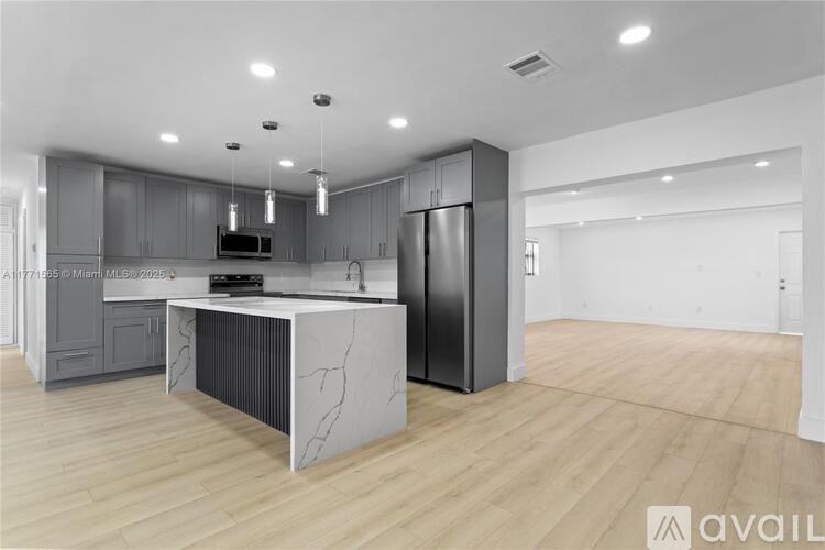 A modern kitchen with a central island and a refrigerator to the right.