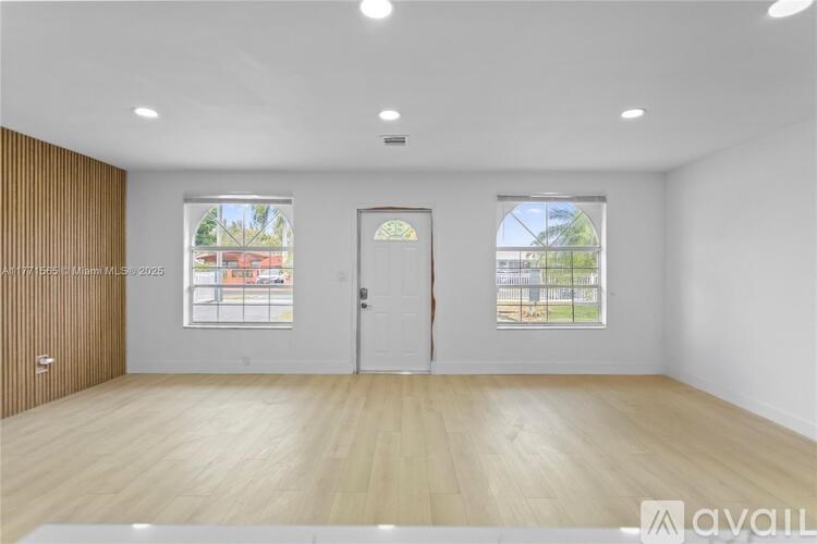 A spacious room with wooden flooring and two windows.