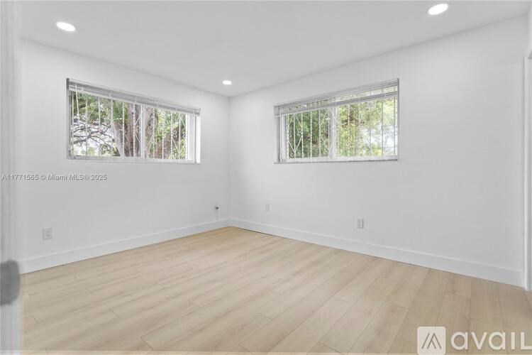 A spacious room with wooden flooring and two windows.