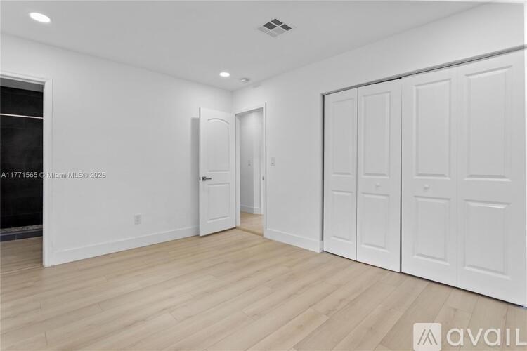 A room with white walls and wooden flooring, featuring a fireplace and a set of white doors.