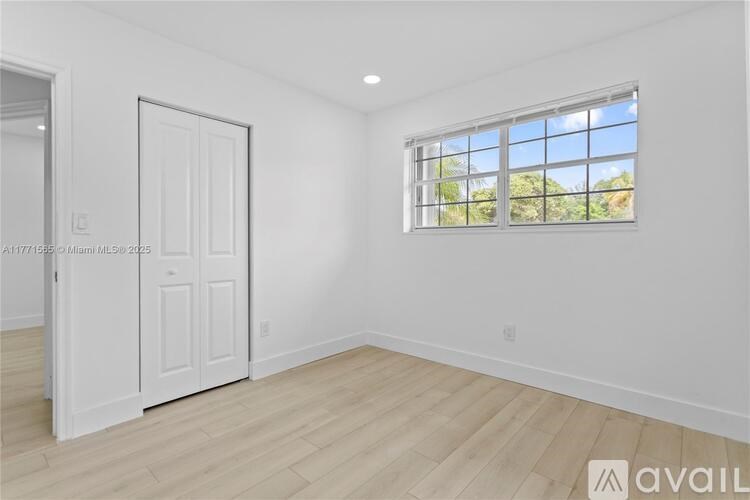 A room with a white door and a window with a view of trees outside.