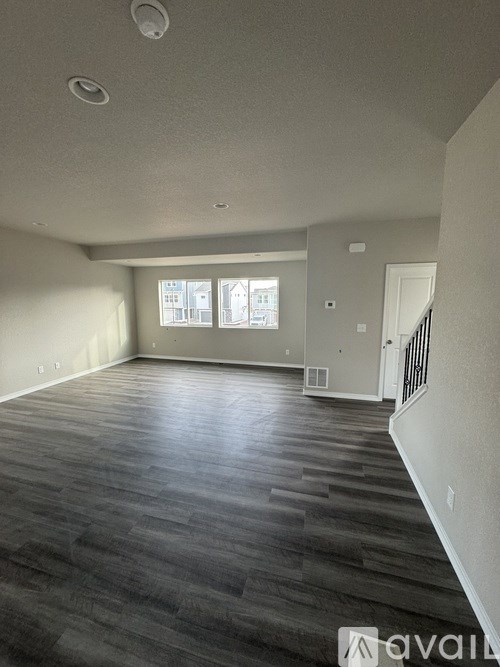 A spacious room with wooden flooring and a window with blinds.