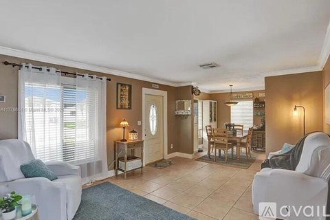 A living room with a white couch, a table with a lamp, and a dining area with chairs.