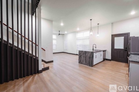 A spacious room with wooden flooring and a staircase with black railings.