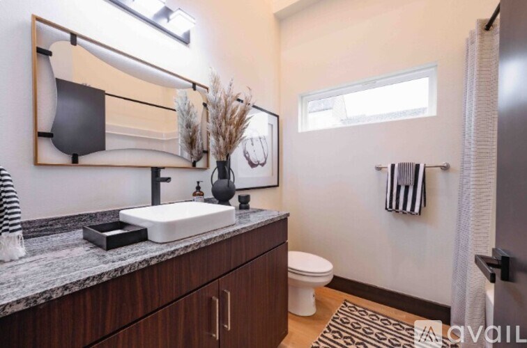 A bathroom with a sink, mirror, toilet, and a rug.