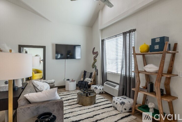 A living room with a grey couch, a wooden ladder, a black and white striped rug, and a television on the wall.
