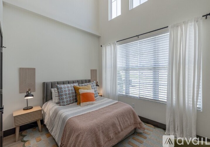 A bedroom with a bed, nightstand, and window with white curtains.