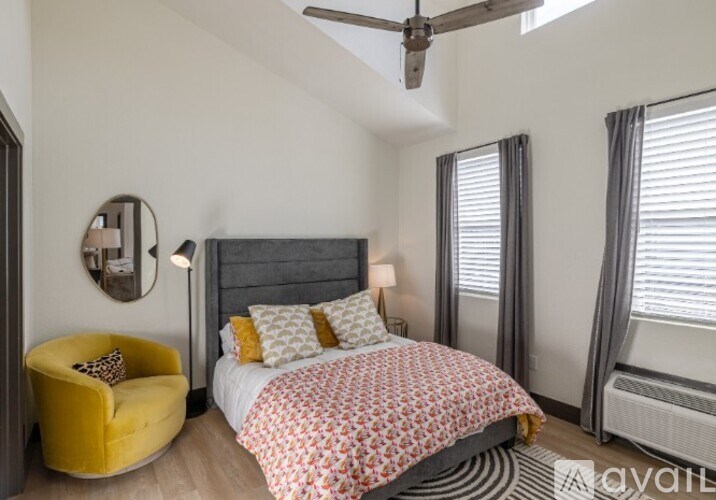 A bedroom with a bed, a yellow chair, and a ceiling fan.