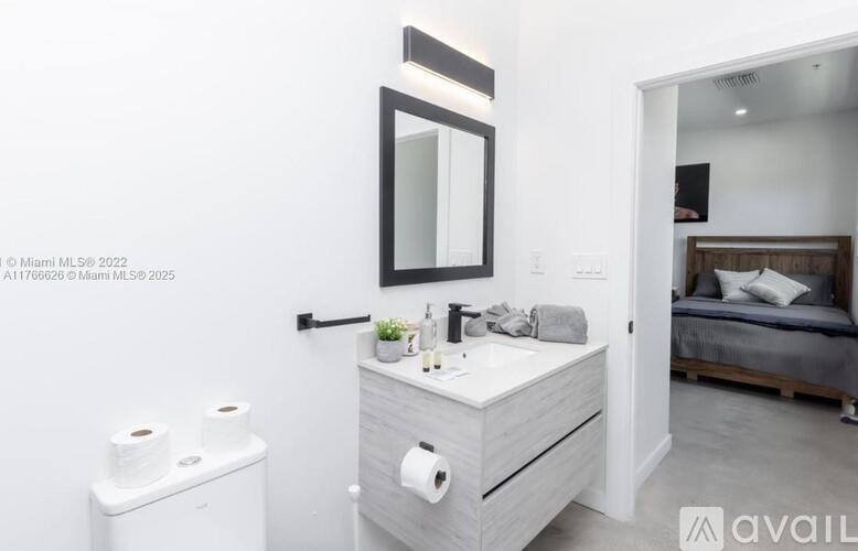 A bathroom with a toilet, sink, mirror, and a bed in the background.