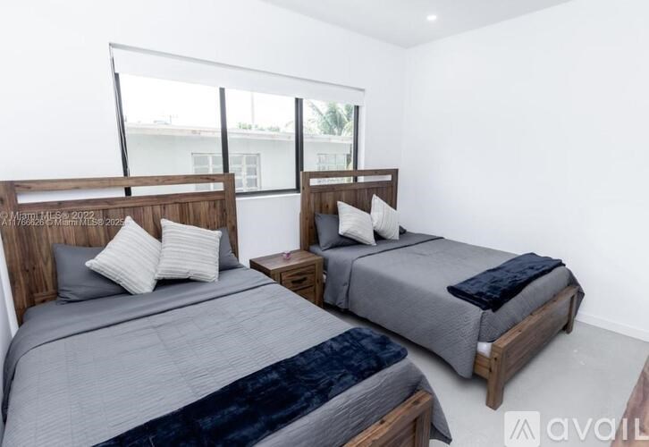 Two beds with grey bedspreads and pillows in a room with white walls.