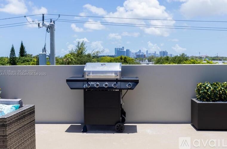 A barbecue grill is on a balcony with a city skyline in the background.