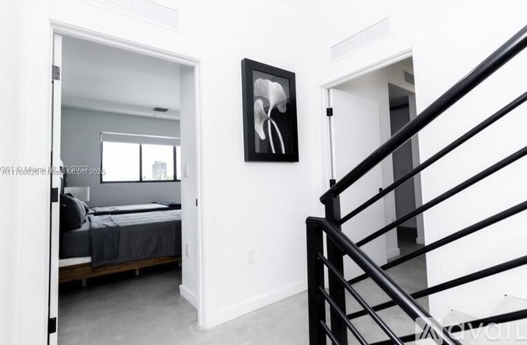 A black and white photo of a woman is hanging on a white wall above a bed in a bedroom.