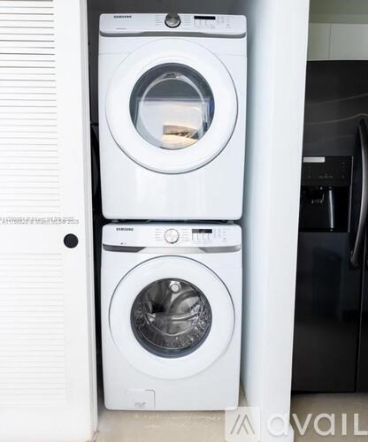 A white front load washing machine with a black dishwasher in the background.