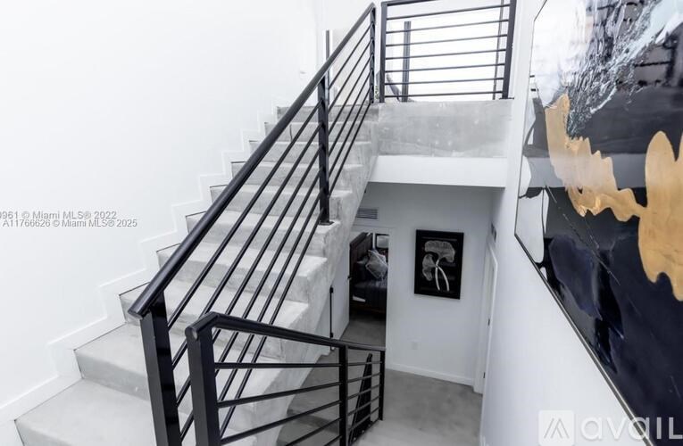 A staircase with a black railing and a white wall with a picture frame.