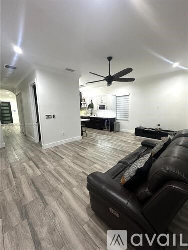 A living room with a black leather couch and a ceiling fan.