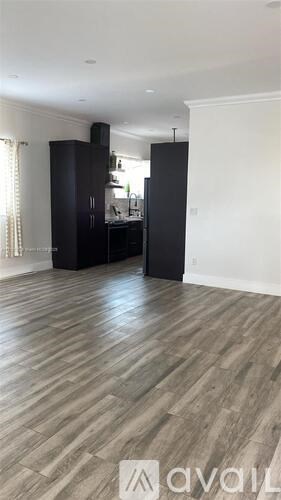 A spacious room with wooden flooring and a kitchen area with black cabinets.