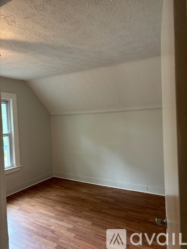 A room with wooden flooring and a window on the left side.