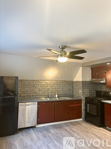 A kitchen with a black refrigerator, a black stove, and a ceiling fan with lights.