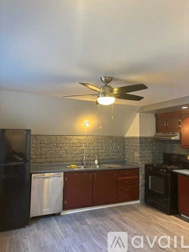 A kitchen with a black refrigerator, a black stove, and a ceiling fan with lights.
