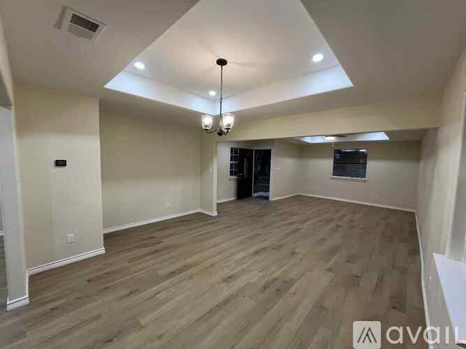 A spacious room with wooden flooring and a chandelier hanging from the ceiling.