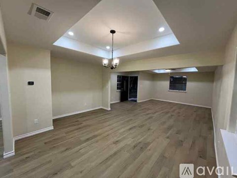 A spacious room with wooden flooring and a chandelier hanging from the ceiling.