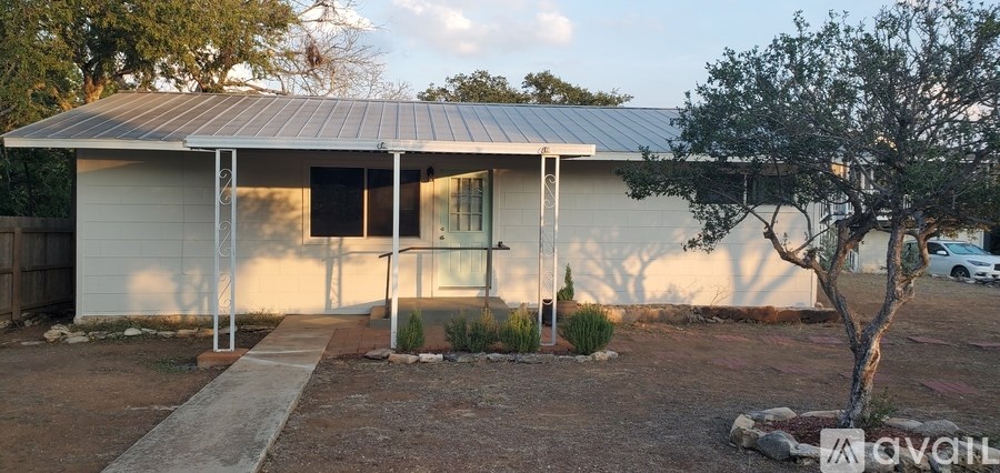 A small white house with a metal roof and a tree in front.