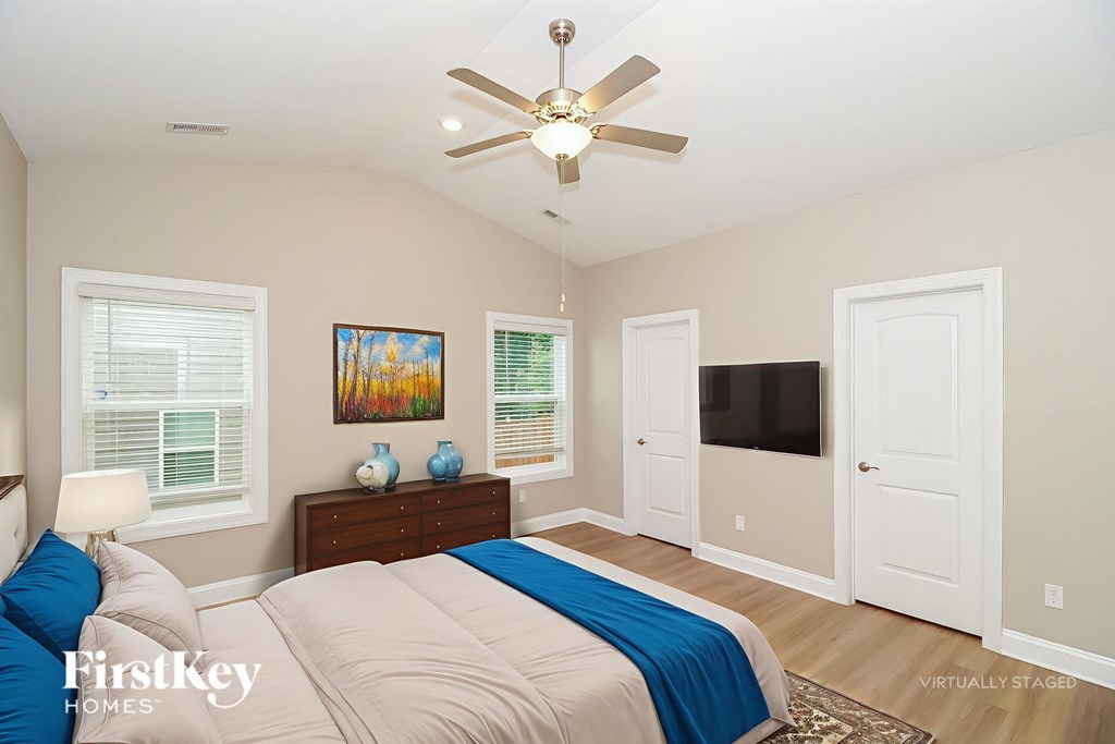 A bedroom with a bed, a ceiling fan, and a painting on the wall.