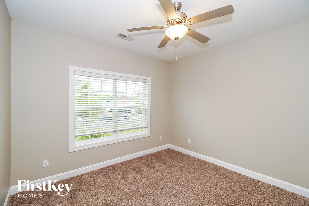 A room with a carpeted floor, a ceiling fan, and a window with blinds.