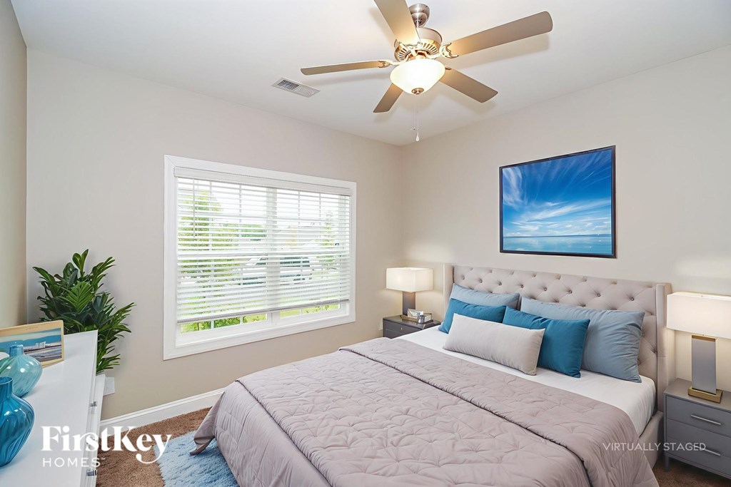 A bedroom with a bed, a ceiling fan, and a painting on the wall.