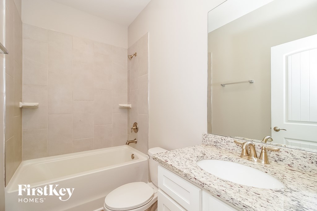 A white bathroom with a marble counter top and a white toilet.