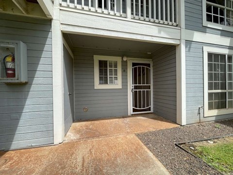A grey house with a white door and a window with bars.