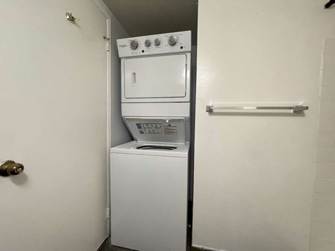 A white dryer and washer are stacked on top of each other in a small laundry room.