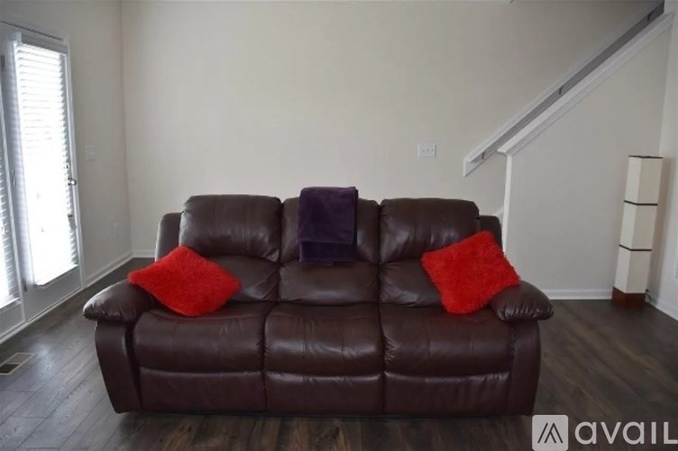 A brown leather couch with two red pillows sits in a room.