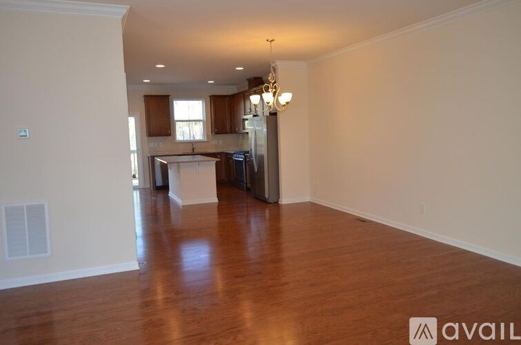 A spacious living room with hardwood floors and a kitchen in the background.