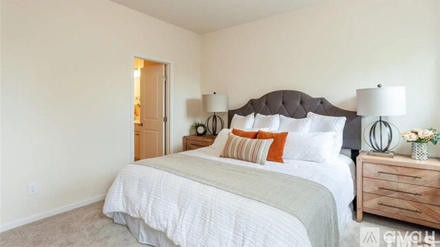 A bedroom with a large bed, a nightstand with a lamp, and a wooden dresser.