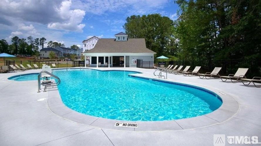 A large swimming pool with a building in the background and lounge chairs around the pool.