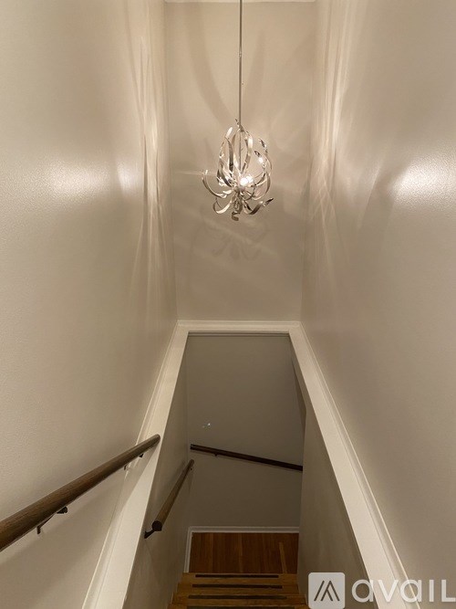 A chandelier hangs from the ceiling in a white hallway.