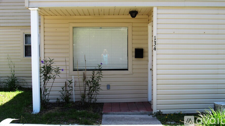 A house with a white pillar and a window with blinds.