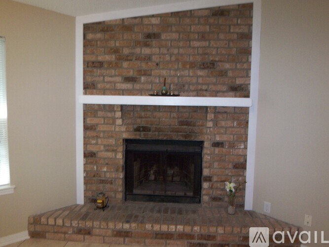 A brick fireplace with a white mantle and a flower on the mantle.
