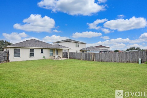 A grassy backyard with a house and a fence.