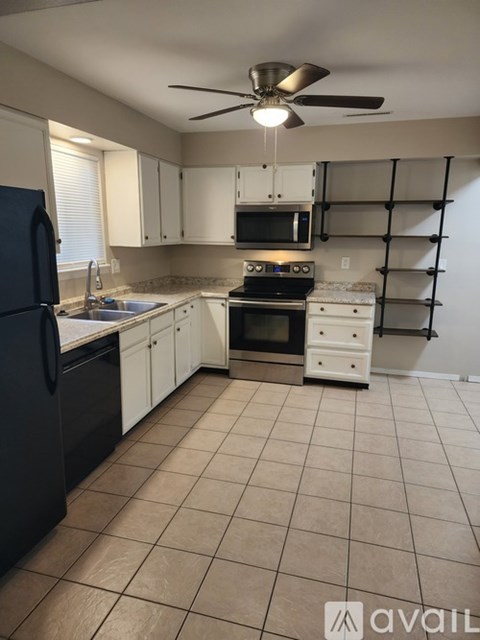 A kitchen with a black fridge, white cabinets, and a fan.