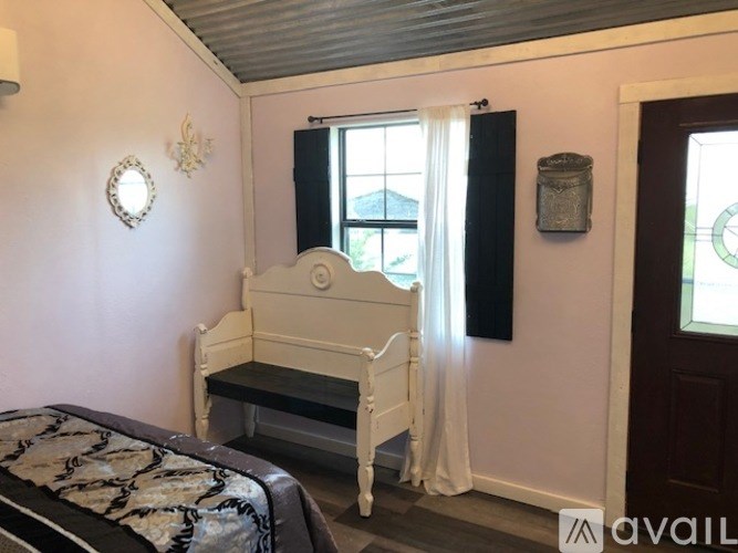 A white bed with a black and white bedspread is in a room with a white bedside table and a window with white curtains.