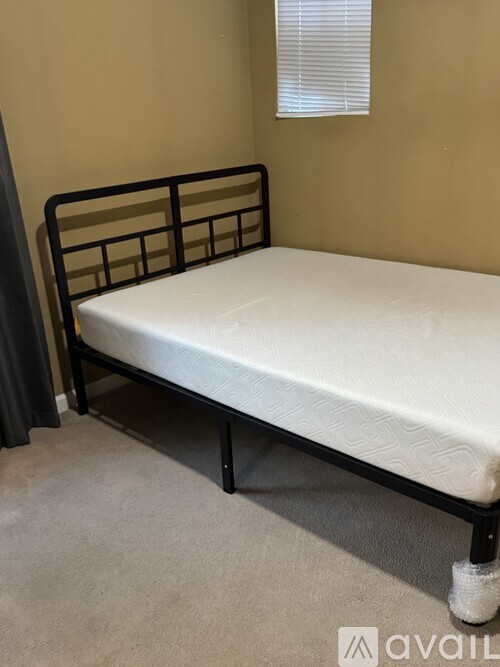 A white mattress with a black metal frame is on a beige carpeted floor.
