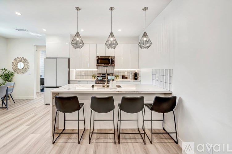 A modern kitchen with a white island and four brown chairs.