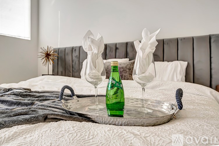 A tray with a green bottle, two glasses, and a brush on a bed.