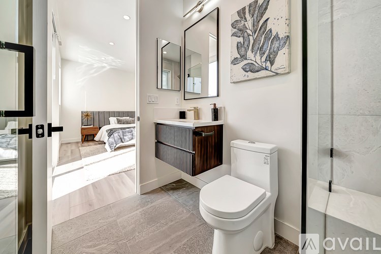 A white toilet is in a bathroom with a mirror and a painting on the wall.