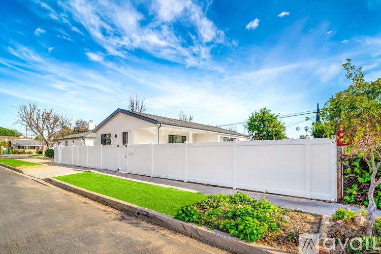 A white house with a white fence and green bushes in front.