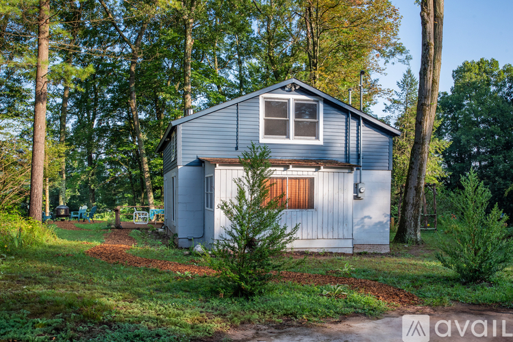 A blue house with a white door and windows is surrounded by trees.