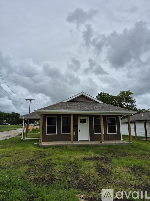 A small house with a brown roof and a white door is in the foreground with a cloudy sky above.